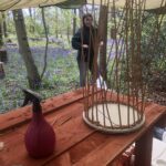 A plank basket starting, on a table in our South London Woods with a woman smiling and bluebells flowering.