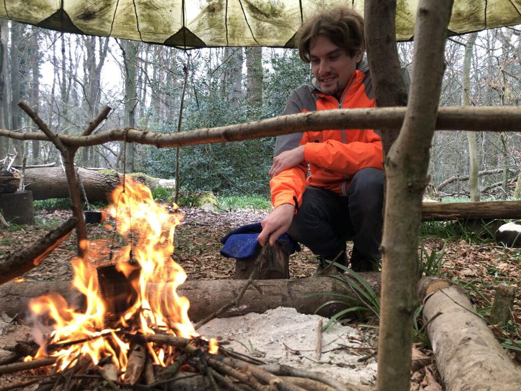 Man smiling with pride in fire and pot suspension system - bringing together the skills learnt over a weekend bushcraft course