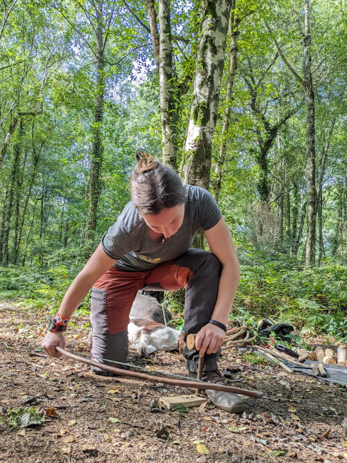 Lizzy Maskey demonstrating Bow Drill, Friction Fire Lighting in a Silver Birch Woodland in Sunshine