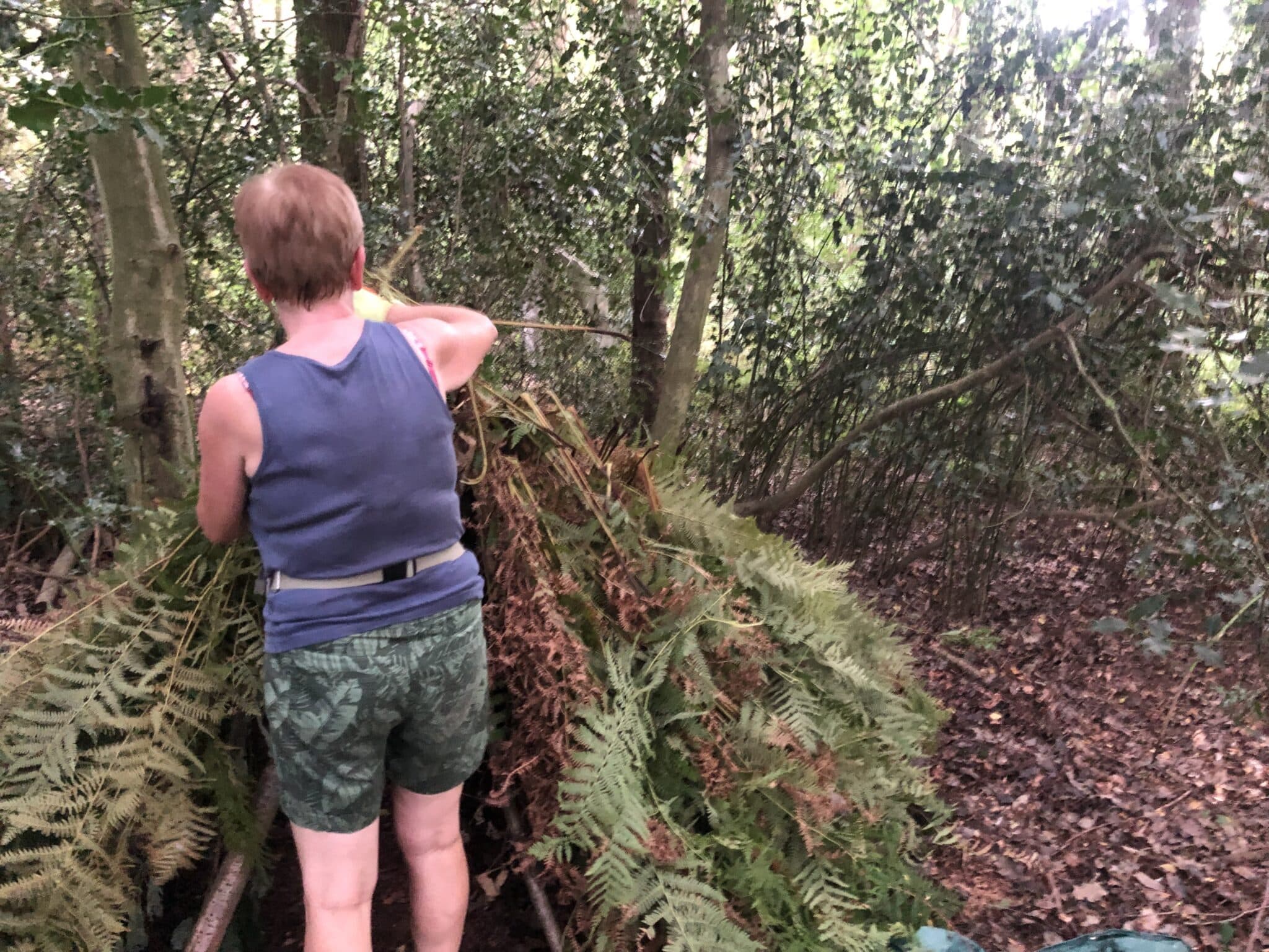 a women in a vest top making a natural debris shelter as part of a weekend bushcraft course