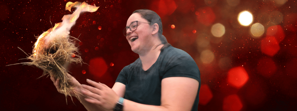 A woman with a huge smile a lit tinder bundle, fire and a christmas gift background