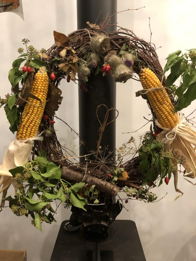 a home made wreath to celebrate harvest decorated in corn on the cob, ivy, ivy flowers and rose hips.