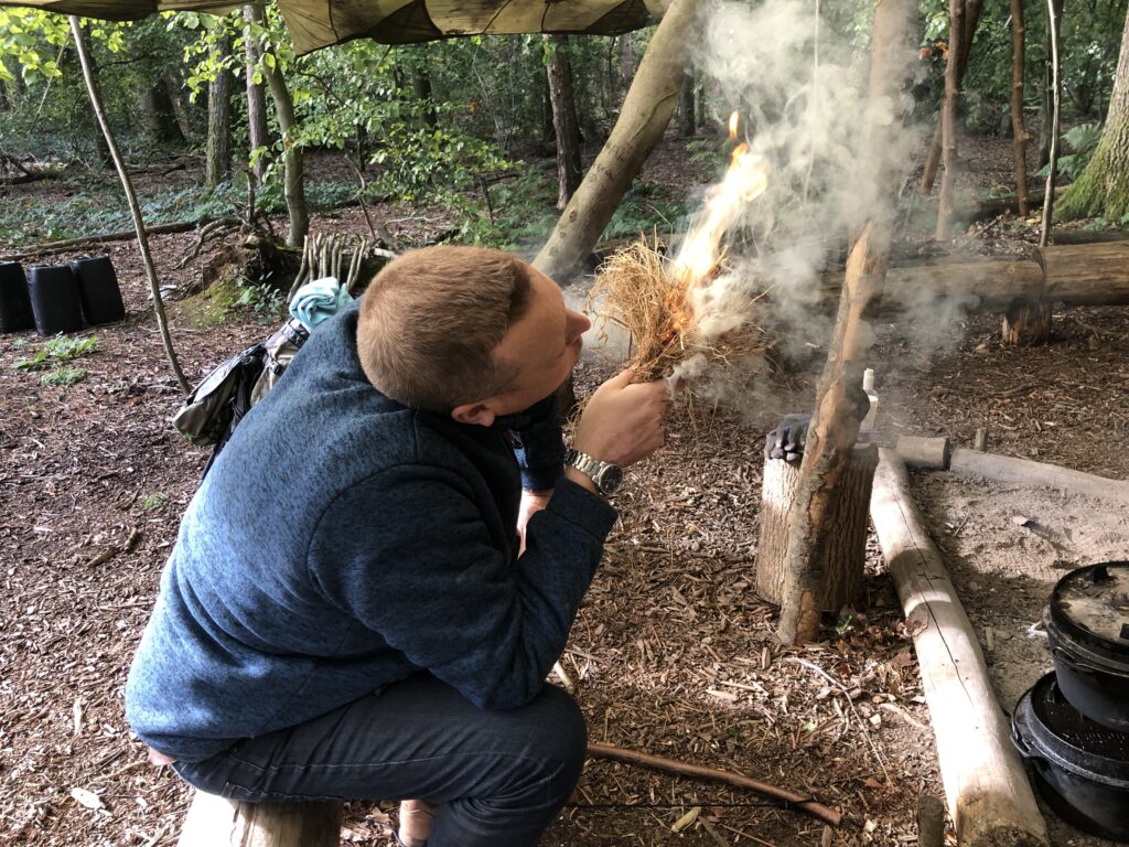 Man blowing into flaming tinder bundle on a weekend bushcraft & survival course