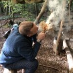 Man blowing into flaming tinder bundle on a weekend bushcraft & survival course