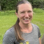 Lizzy Maskey Smiling in a Pippin & Gile Logoed tee in the sunshine with cropped grass behind