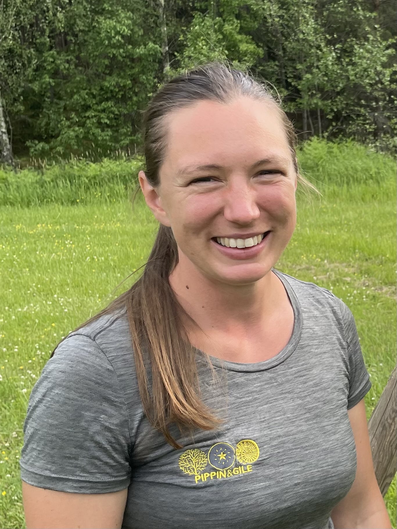 Lizzy Maskey Smiling in a Pippin & Gile Logoed tee in the sunshine with cropped grass behind
