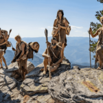 a group of people on a rocky hilltop all wearing Stone Age clothing and posing.